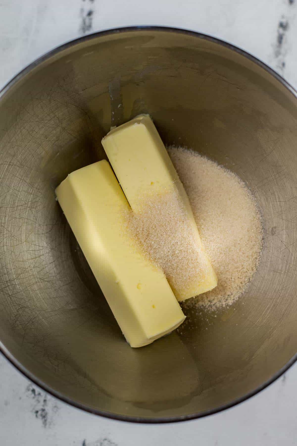 silver mixing bowl with sugar and two sticks of butter.
