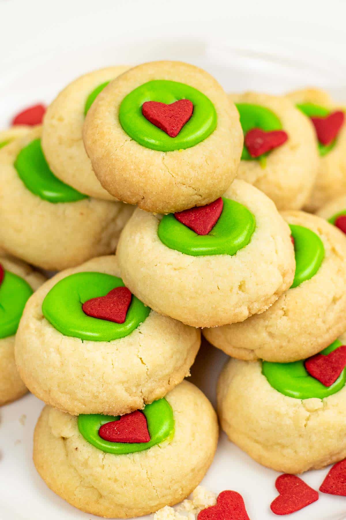 closeup of a stack of shortbread thumbprint cookies with green icing and a red candy heart in the center.