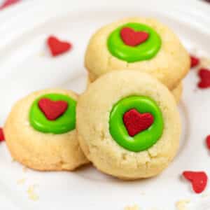 white plate with four vanilla shortbread cookies with green icing and aa red candy heart in the center.