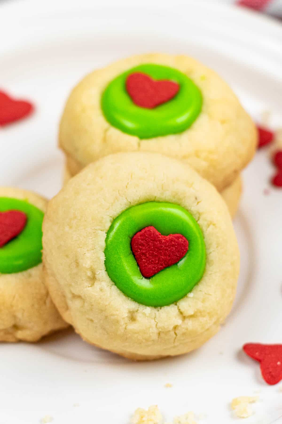 closeup of a vanilla thumbprint cookie with green icing and a little red candy heart in the center.