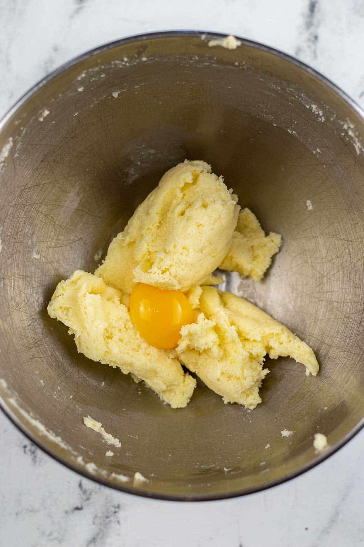 silver mixing bowl with creamed butter and sugar with a raw egg on top.