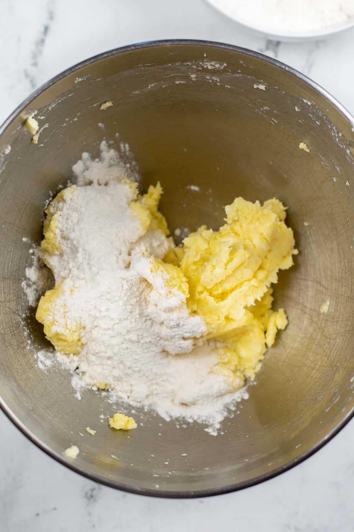 silver mixing bowl with creamed butter and sugar mixture with flour on top.