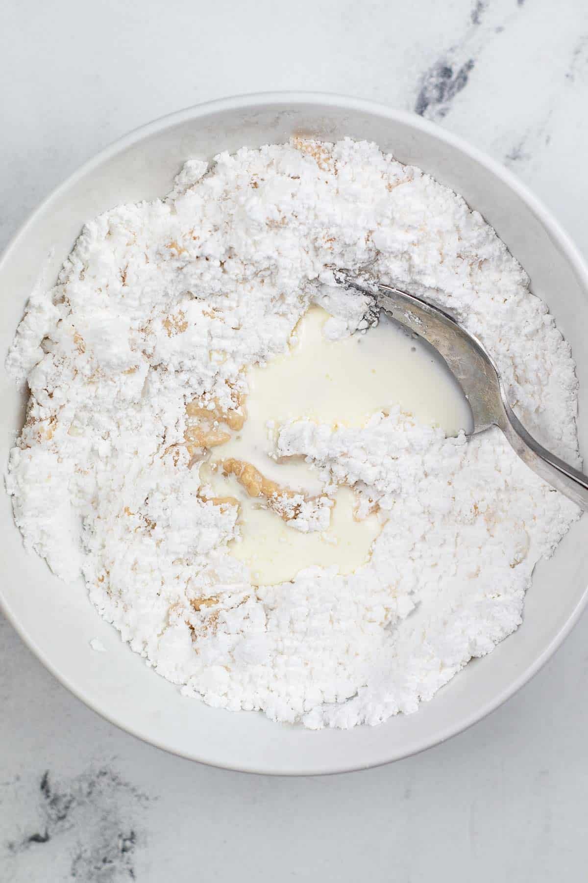 white bowl with powdered sugar being mixed with milk for icing.