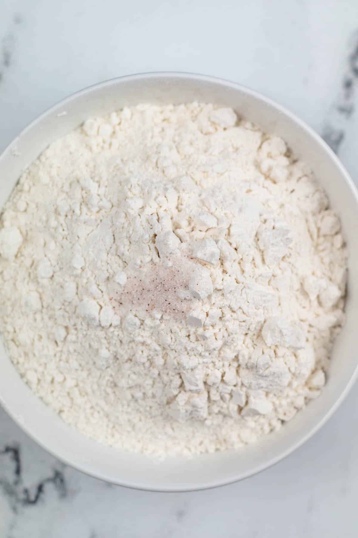 white bowl of flour with pink salt on top.