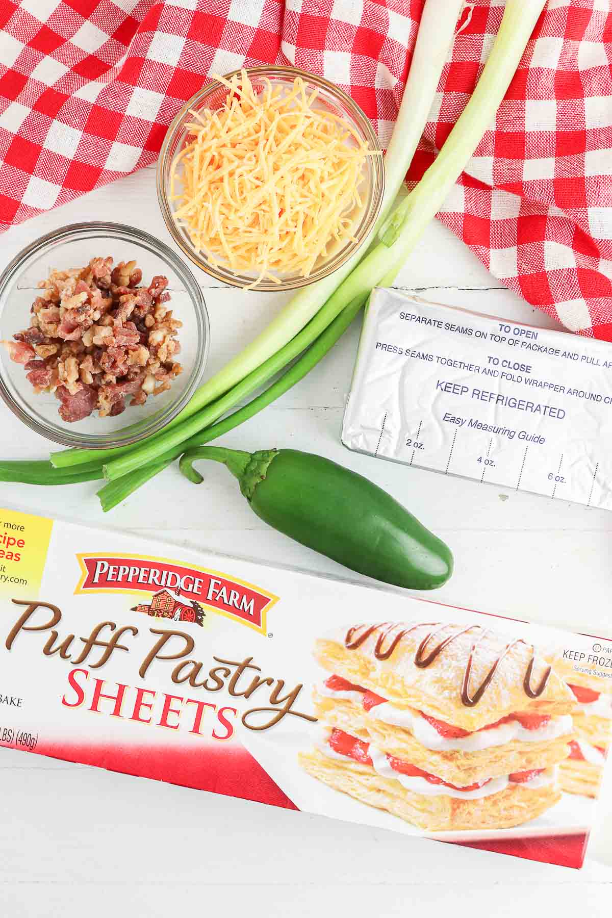 box of pepperidge farm puff pastry dough, block of cream cheese, bowl of bacon bits, bowl of shredded cheese and two green onions.