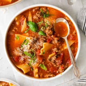 closeup of a white bowl full of lasagna soup in a tomato broth topped with fresh basil.