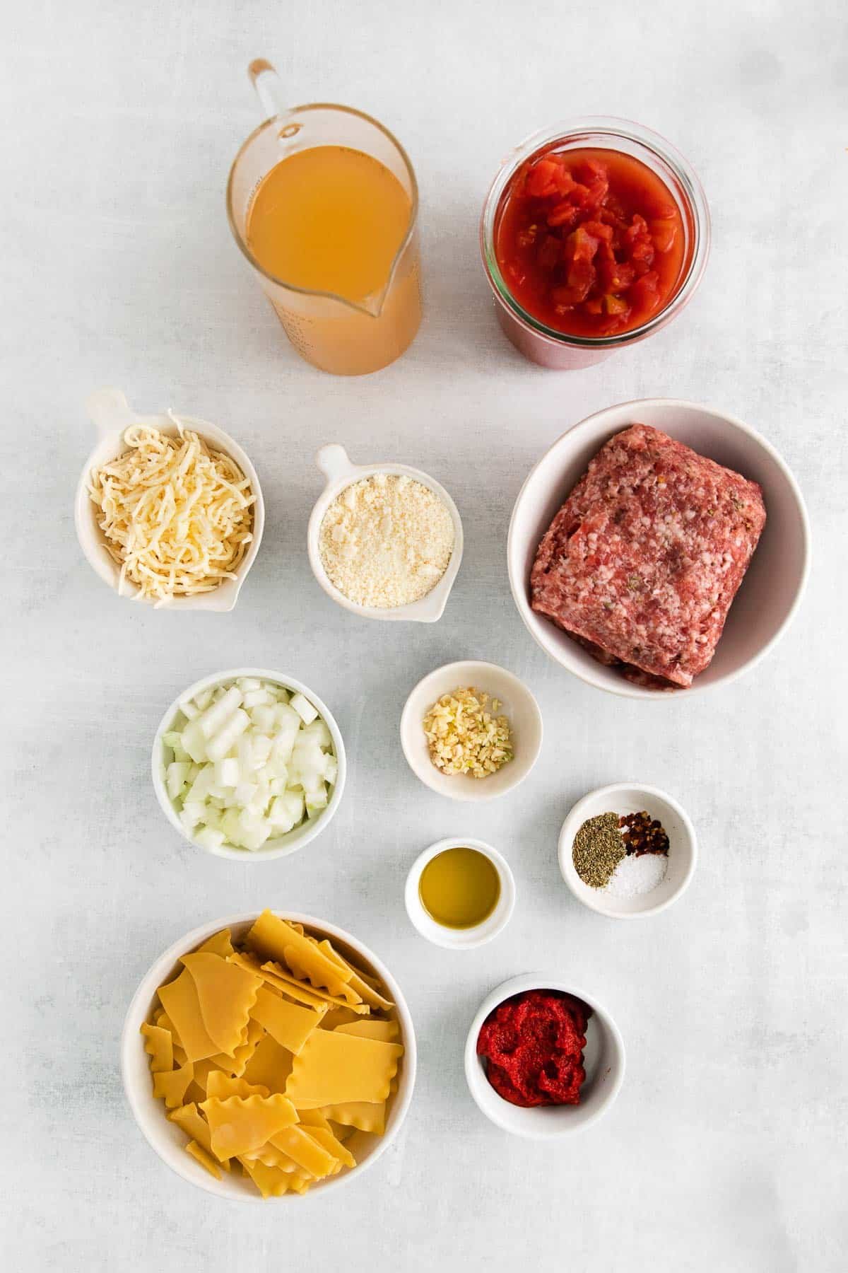 several white bowls with ingredients for lasagna soup - sausage, tomato paste, lasagna noodles, diced onions, garlic, chicken broth, diced tomatoes, cheeses.