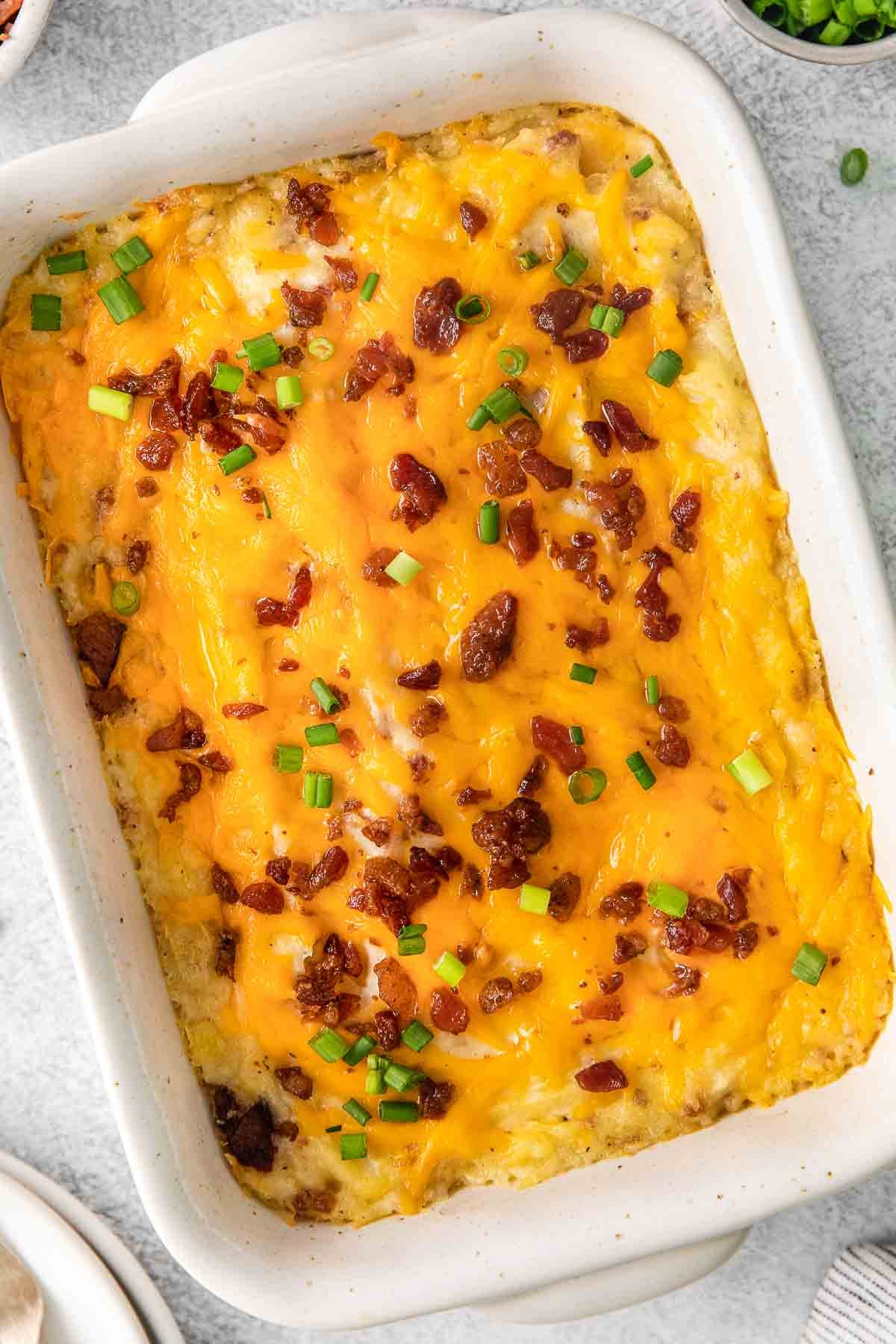 closeup of twice baked potato casserole with cheese and bacon on top in a rectangle dish.