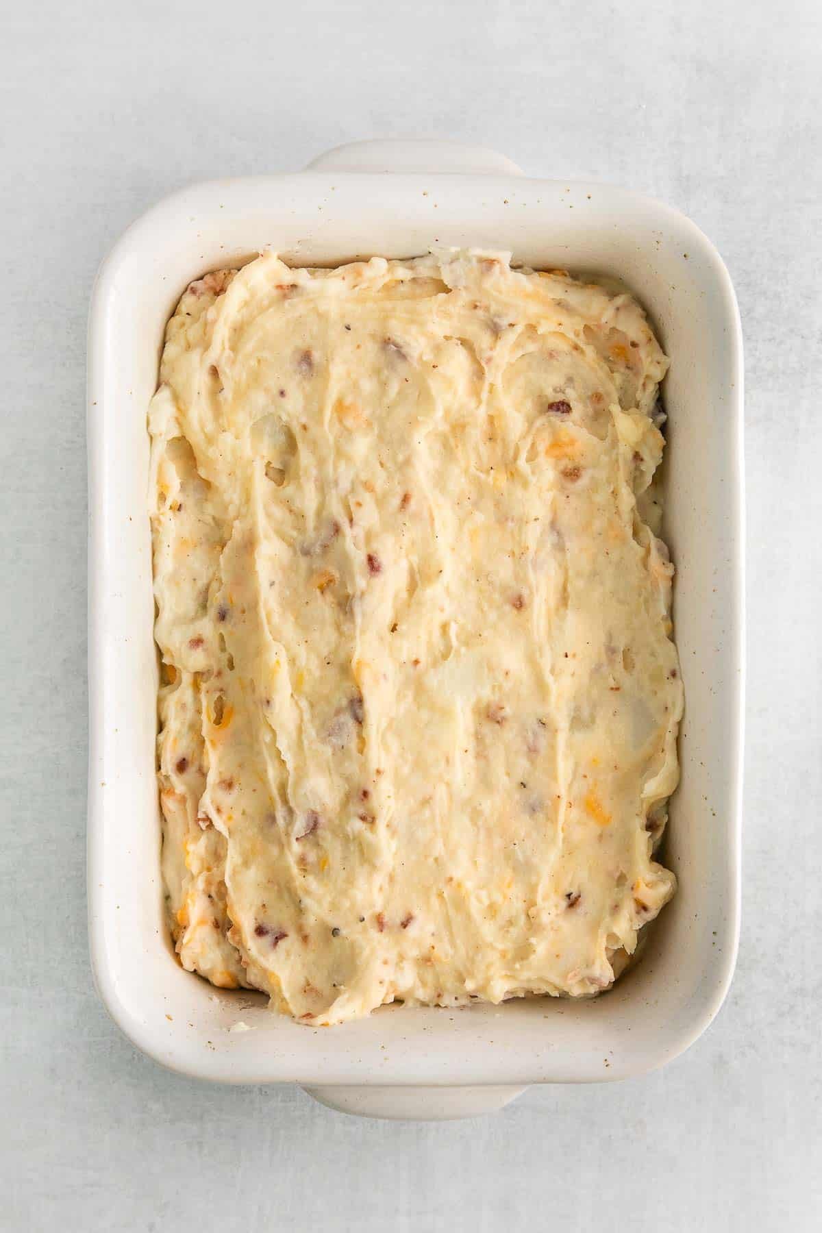 rectangle baking dish with mashed potatoes, cheese and bacon mixture.