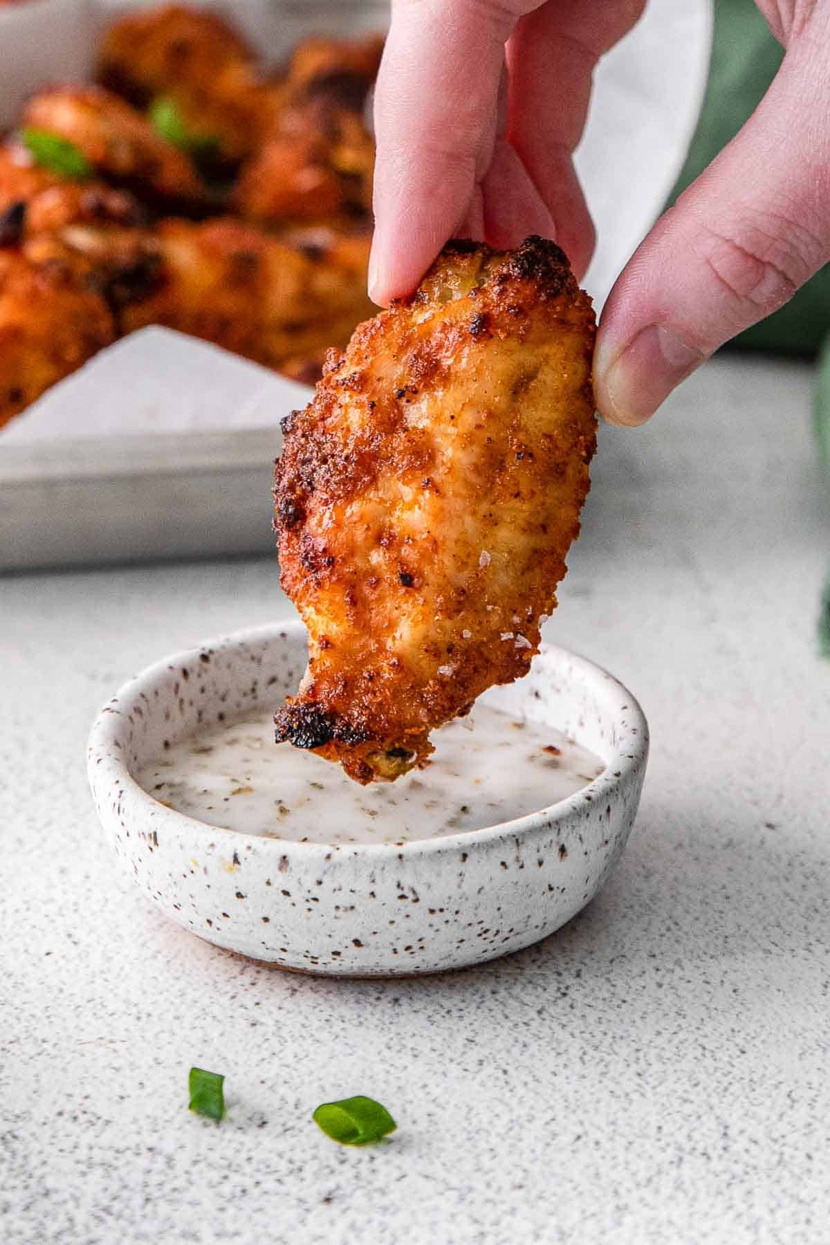 woman's fingers dipping a crispy chicken wing into ranch dresssing.