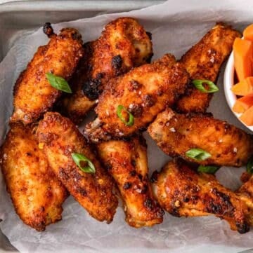 closeup of several crispy chicken wings on white parchment paper.