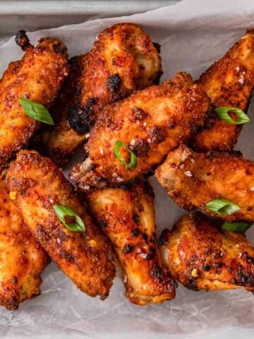 closeup of several crispy chicken wings on white parchment paper.