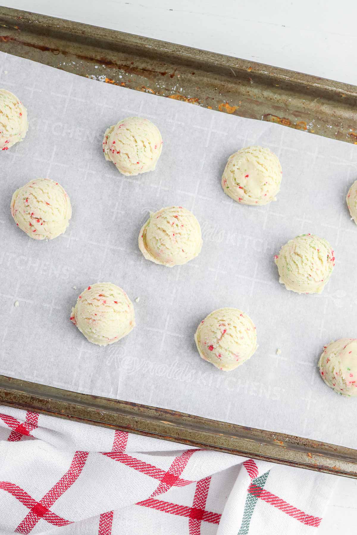 several sugar cookie dough balls on white parchment lined cookie sheet.