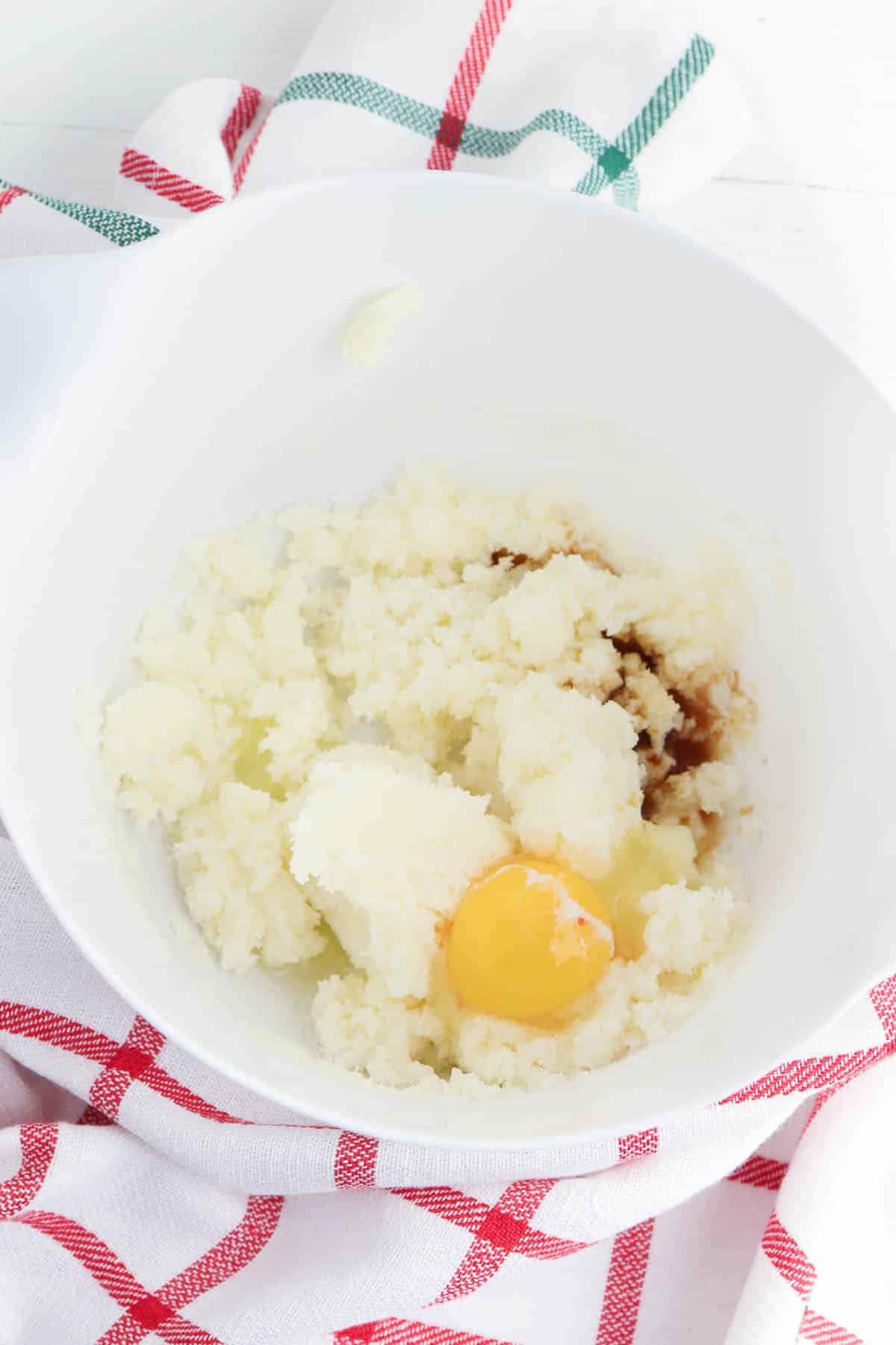 white mixing bowl with brown sugar and butter mixture with a raw egg on top.