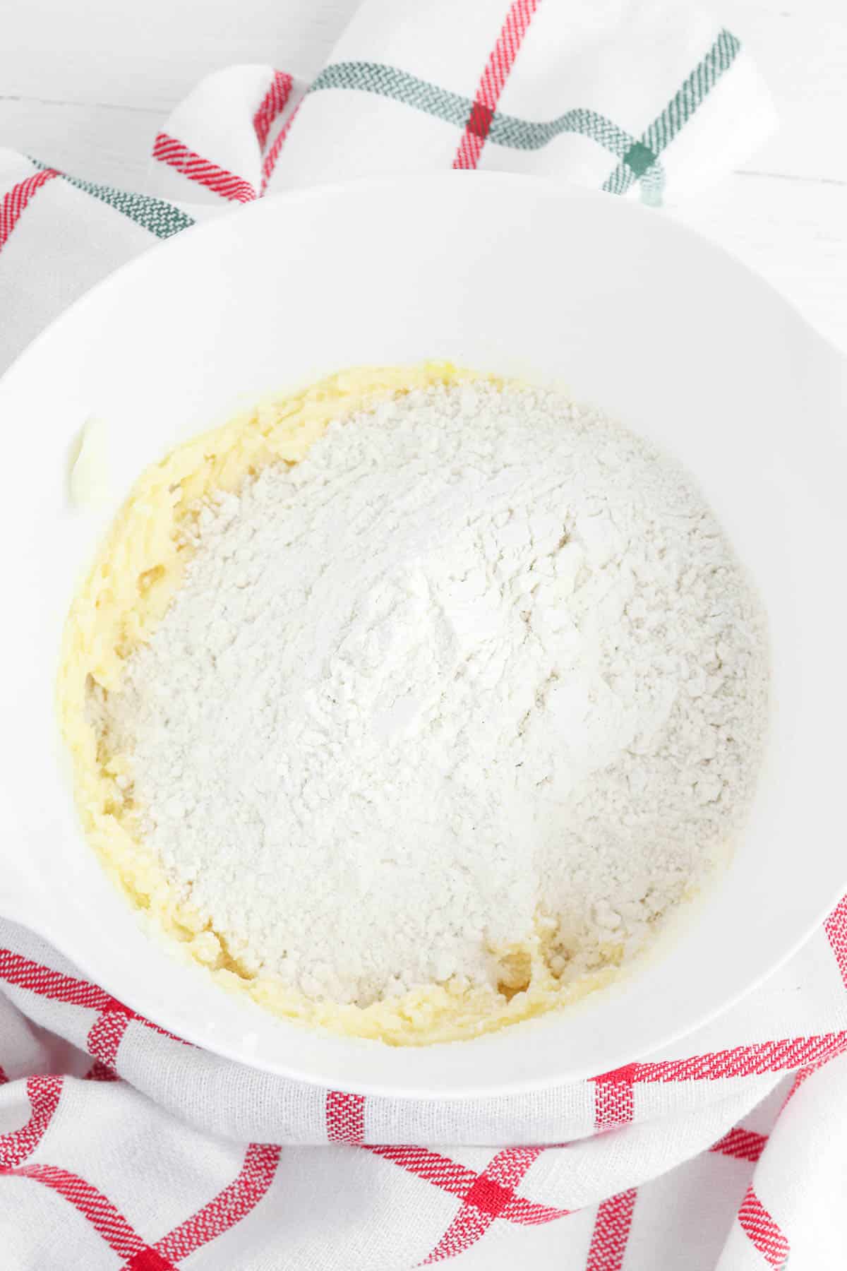 white mixing bowl with flour on top of butter and sugar mixture.