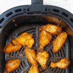 several buffalo chicken wings in a black air fryer basket.