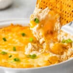 closeup of creamy crab dip being scooped out of a dish with a tortilla chip.