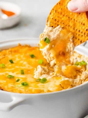 closeup of cheesy hot crab dip being scooped with a tortilla chip.