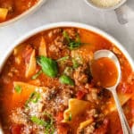 white bowl full of lasagna soup in tomato broth with a spoon on the side.