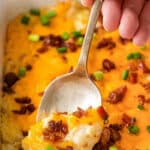 cheesy loaded potato casserole with bacon crumbles being scooped with a spoon.