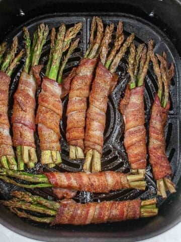 nine bundles of 3 or 4 asparagus spears wrapped in bacon in an air fryer basket.