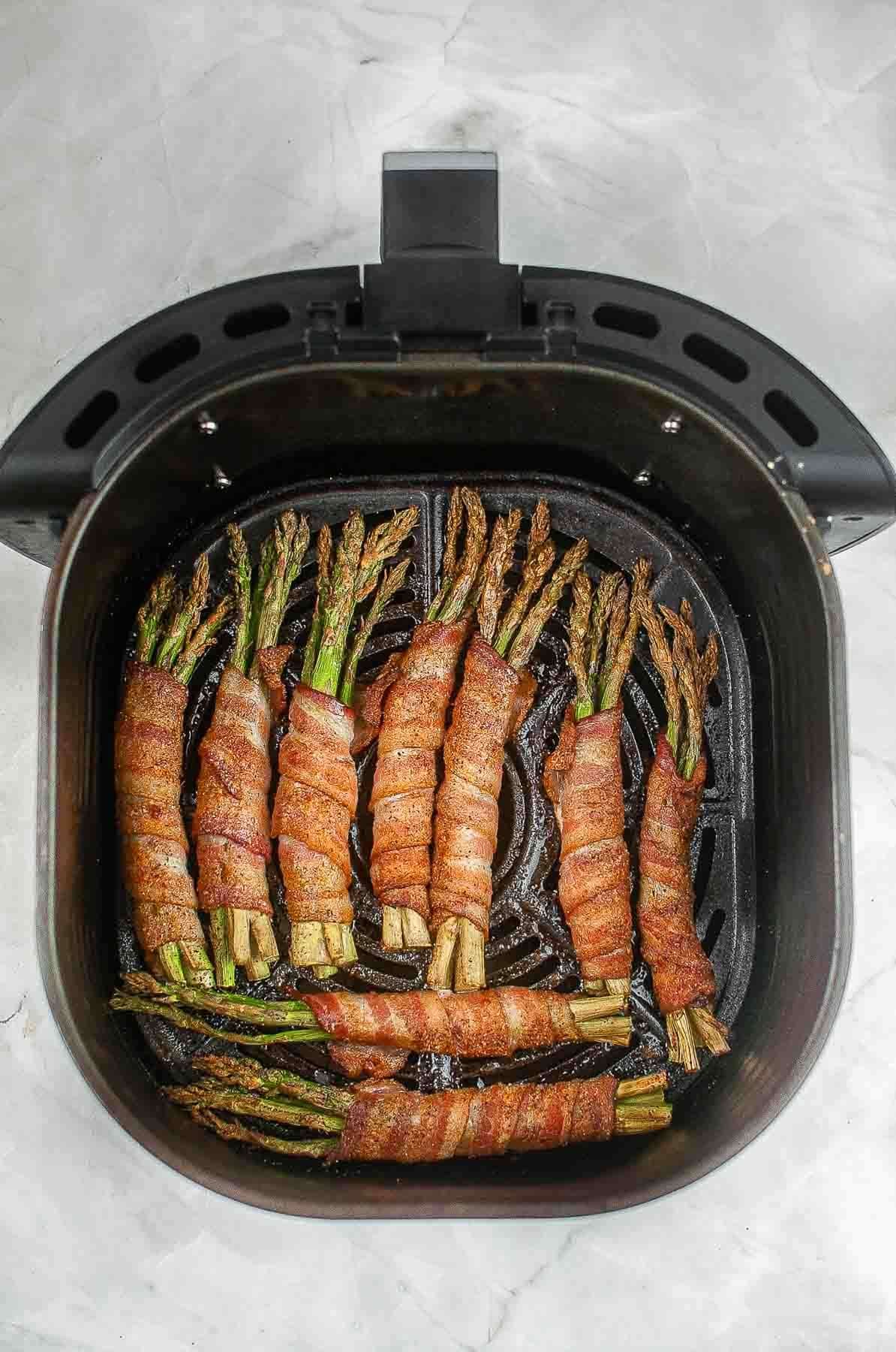 black air fryer basket with nine air fried asparagus wrapped in bacon bundles.