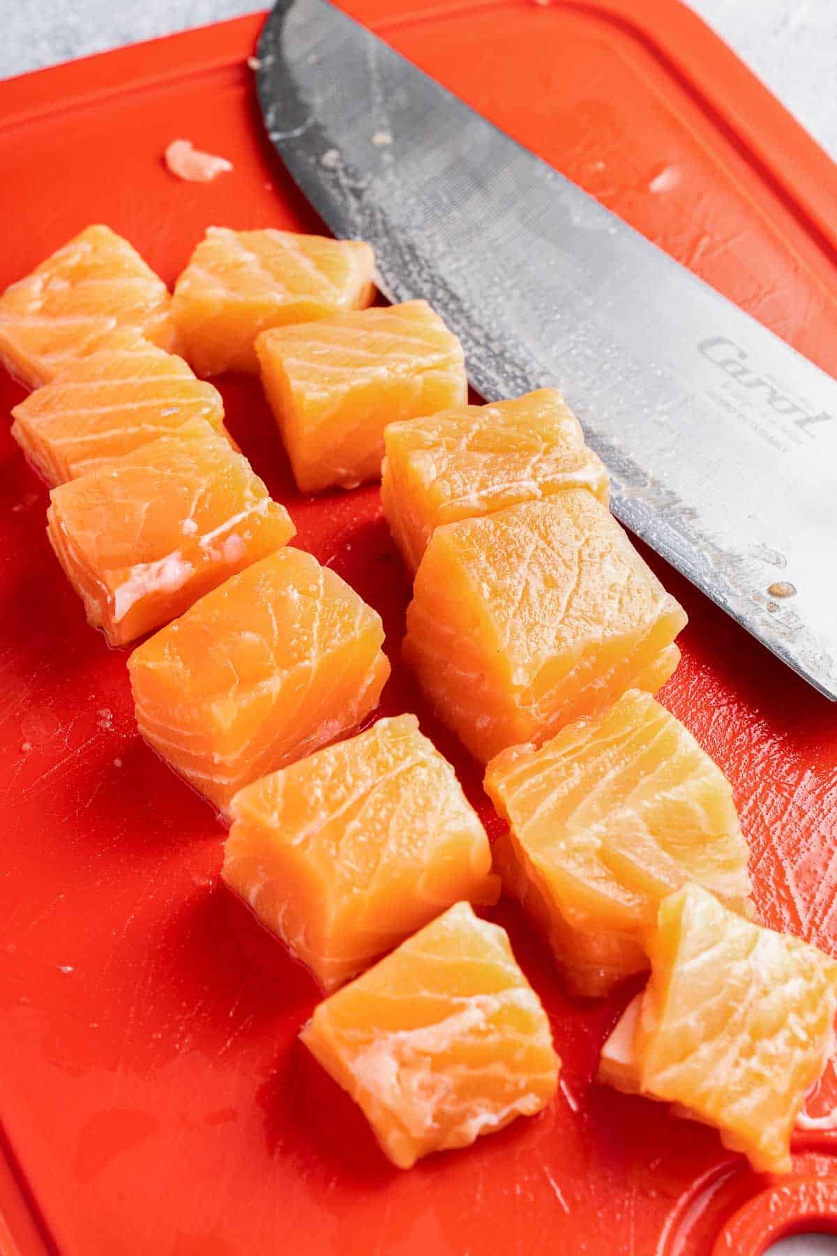 cubes of raw salmon on a red cutting board.