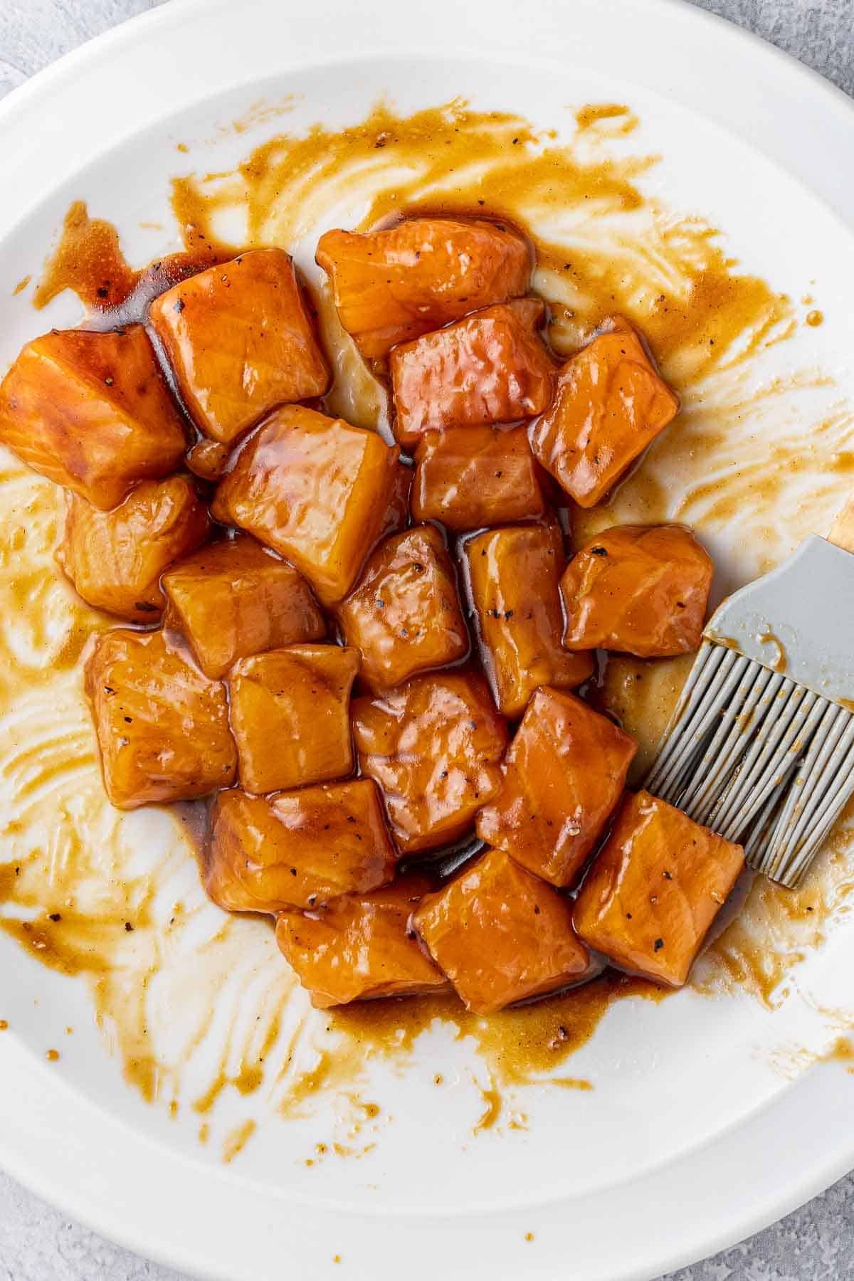 white plate with several cubes of raw salmon in a soy sauce marinade.
