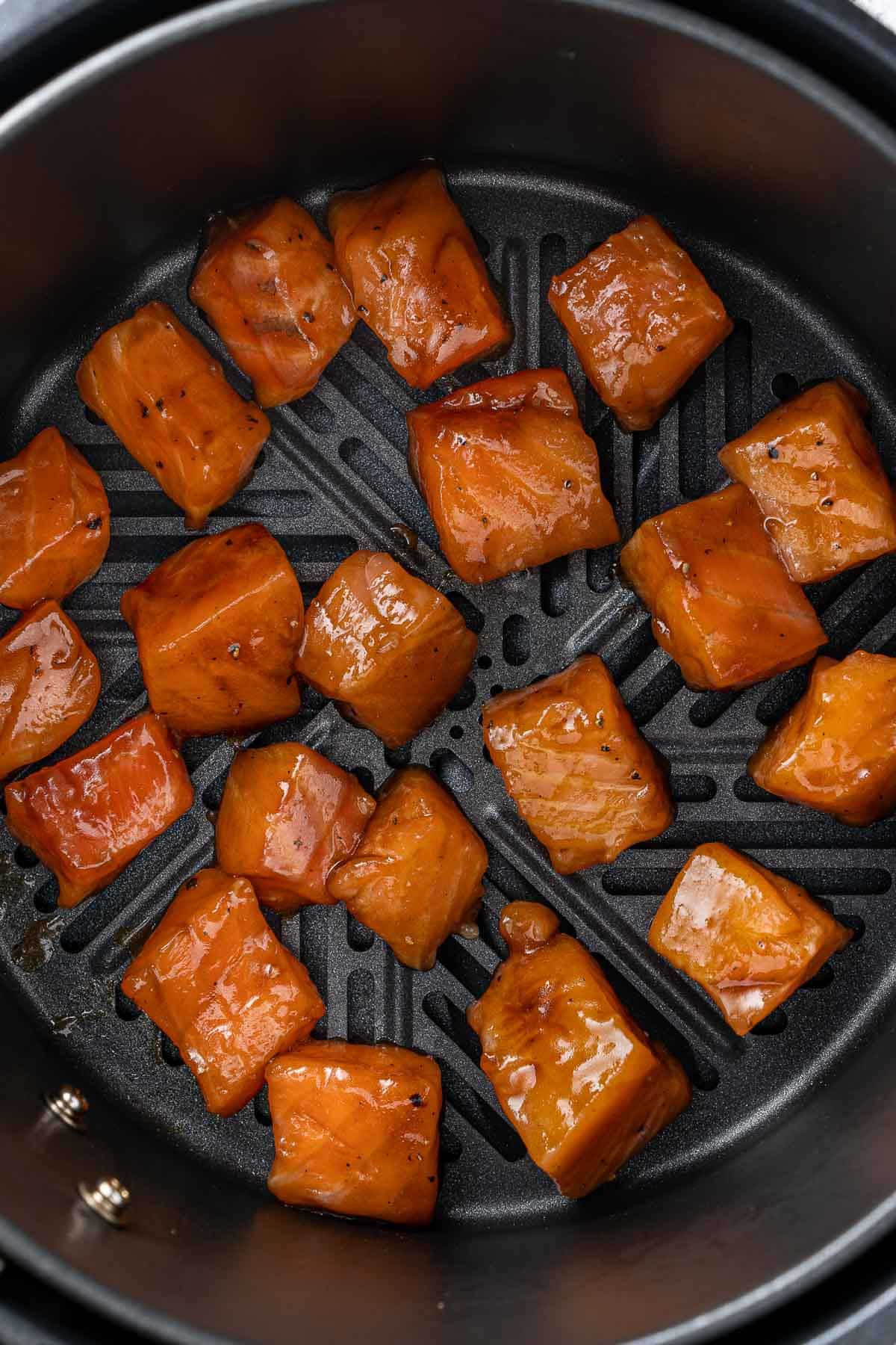 several cubes of raw salmon in a black air fryer.