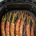 several bundles of bacon wrapped asparagus in an air fryer basket.