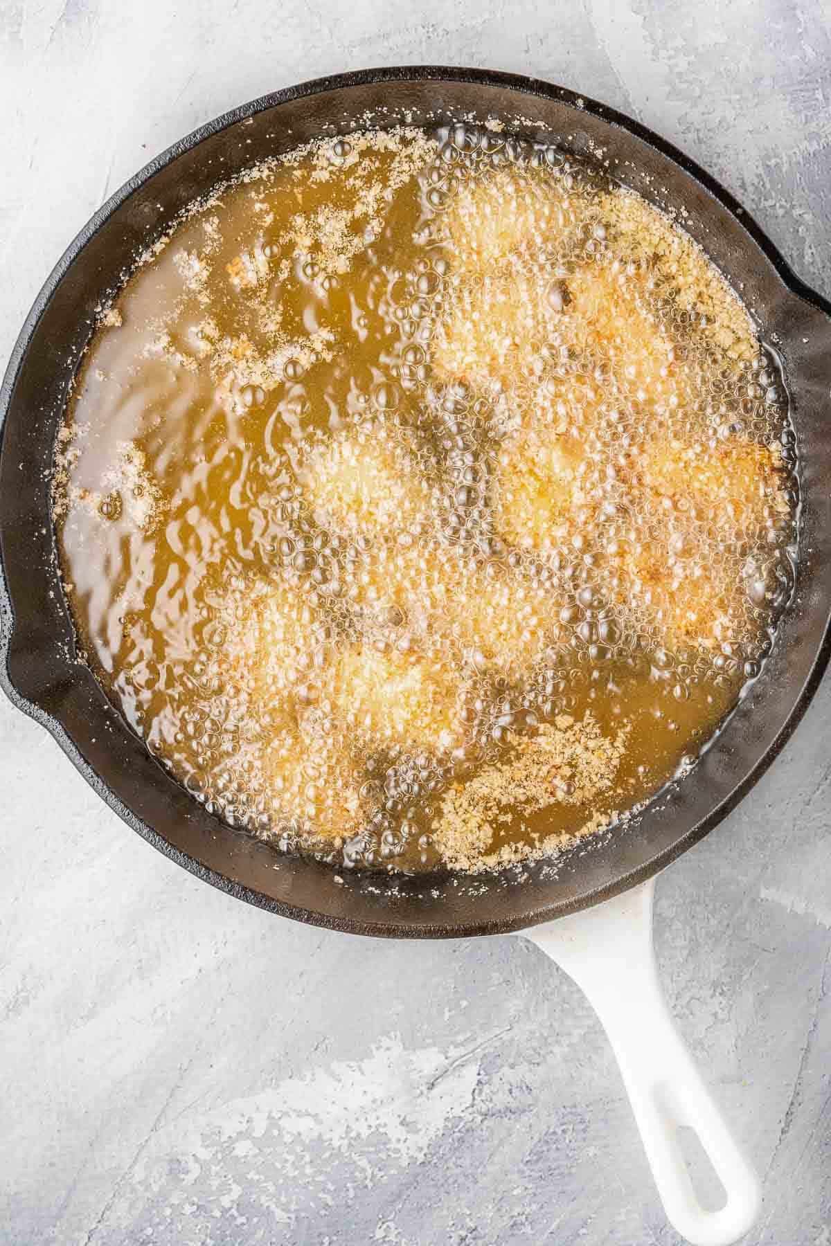 diced cubes of chicken frying in a cast iron pan.