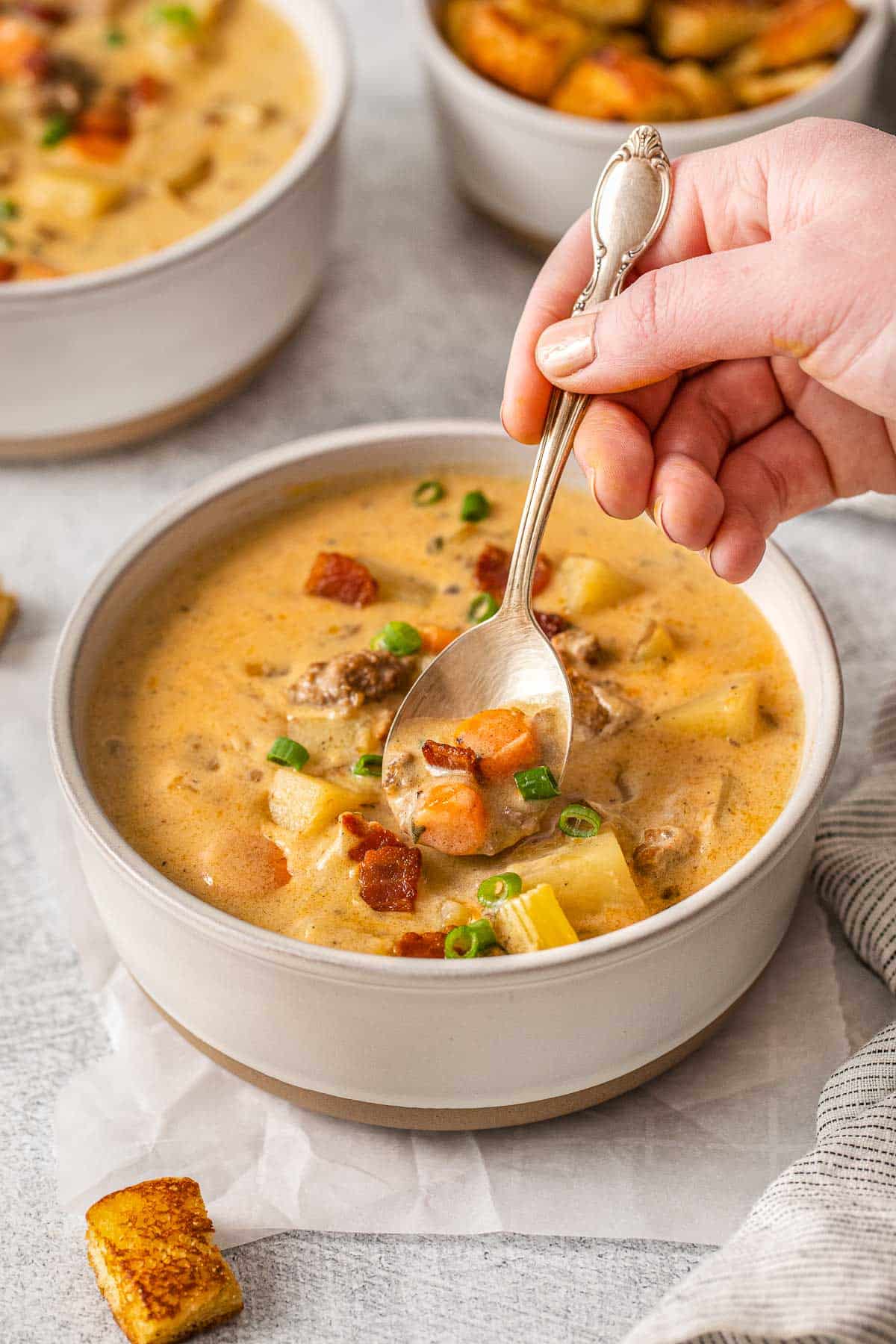 bacon cheeseburger soup with a spoon scooping a bite from a white bowl full.