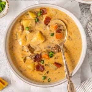 closeup of a bowl full of cheeseburger soup with bacon and potatoes with a antique spoon resting on the side of the bowl.