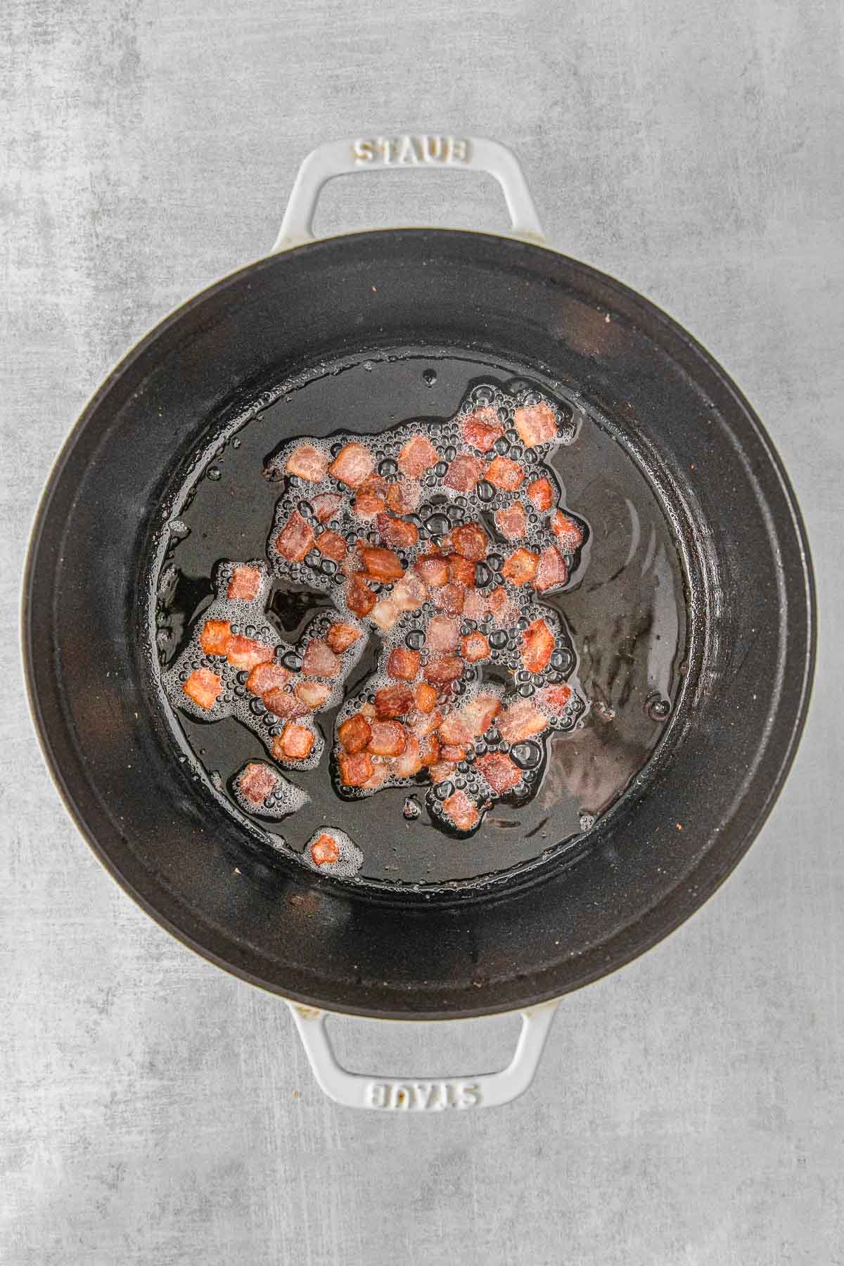 pieces of bacon cooking in a cast iron skillet.