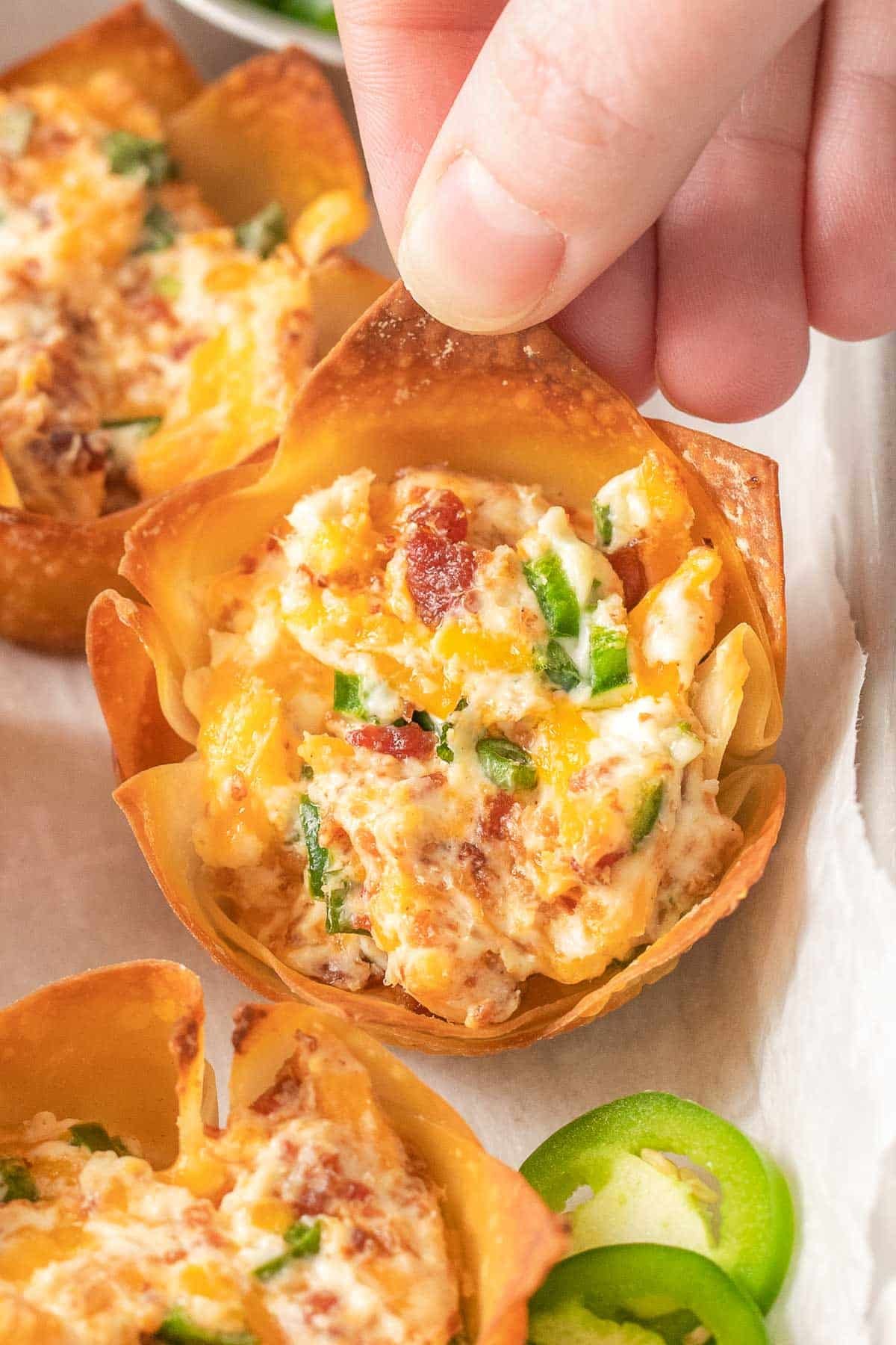 closeup of a jalapeno popper wonton cup being held by a woman's fingers.