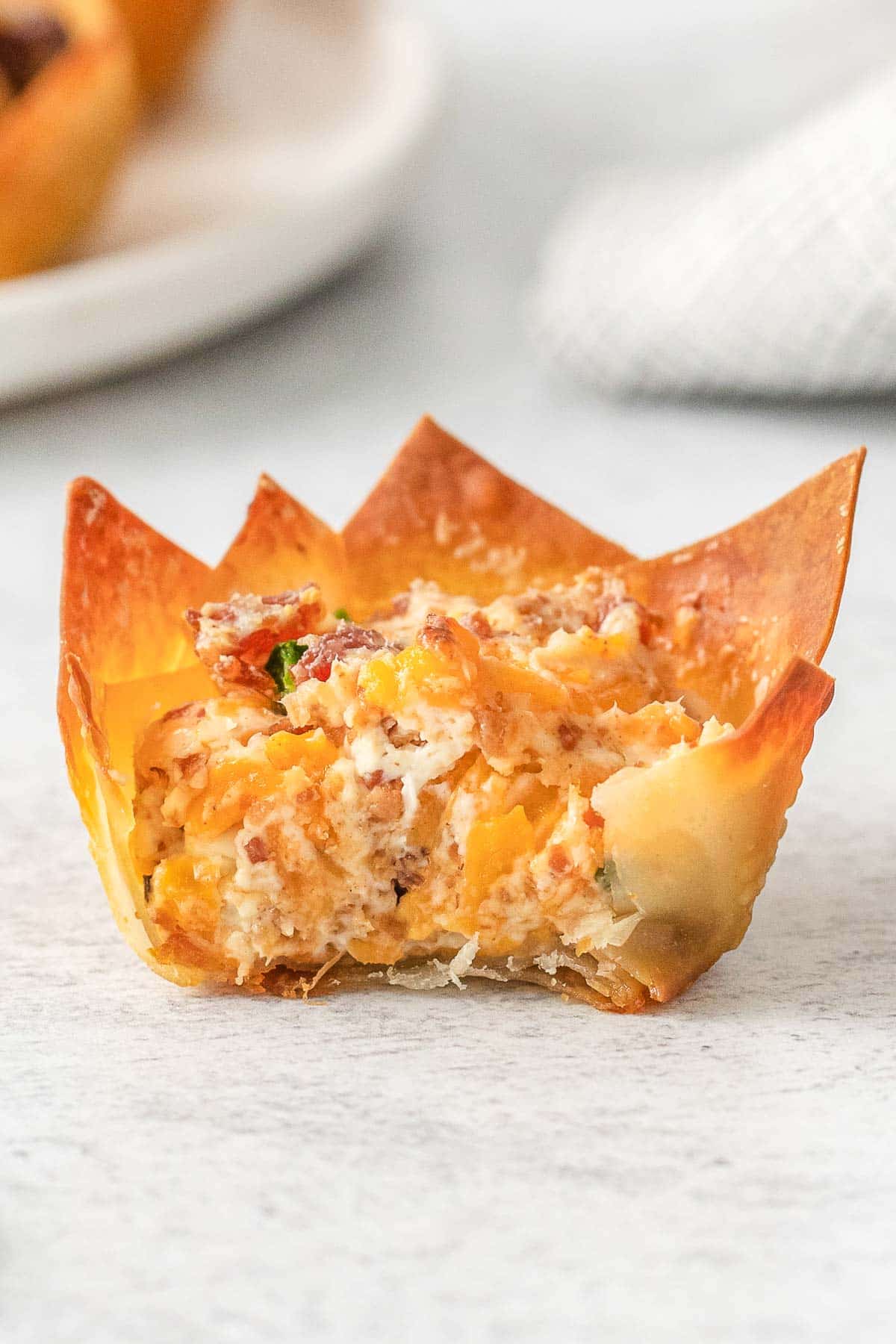closeup of a jalapeno popper wonton cup with a bite taken out of it.