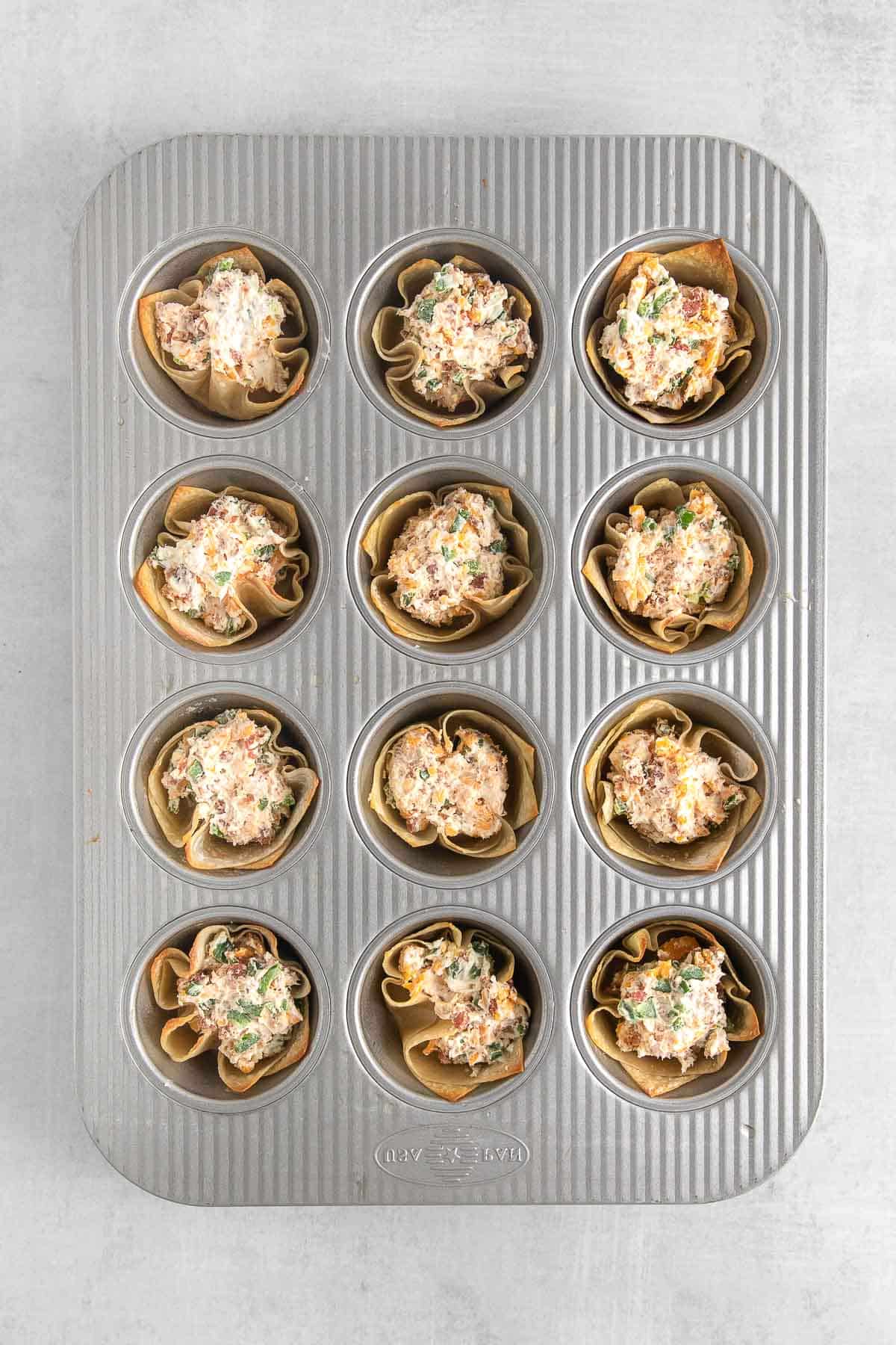 mini muffin tin with wonton wrappers filled with jalapeno popper mixture.