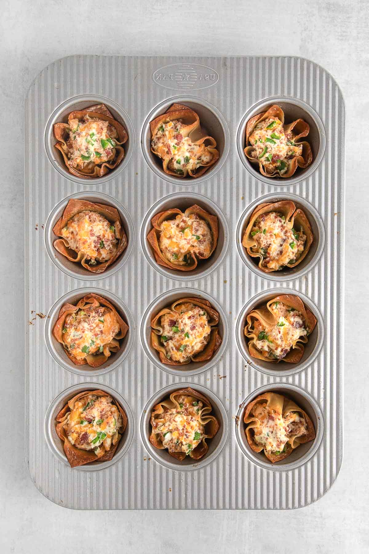 twelve baked jalapeno popper wonton cups in a mini muffin tin.