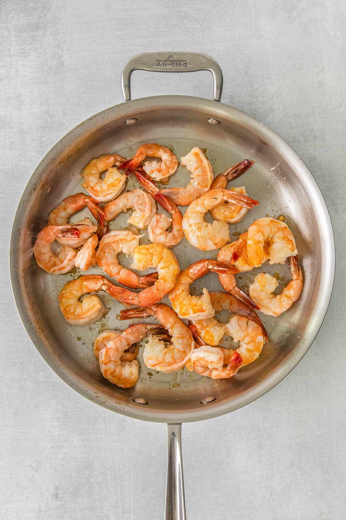 Stainless steel skillet with several cooked shrimp.