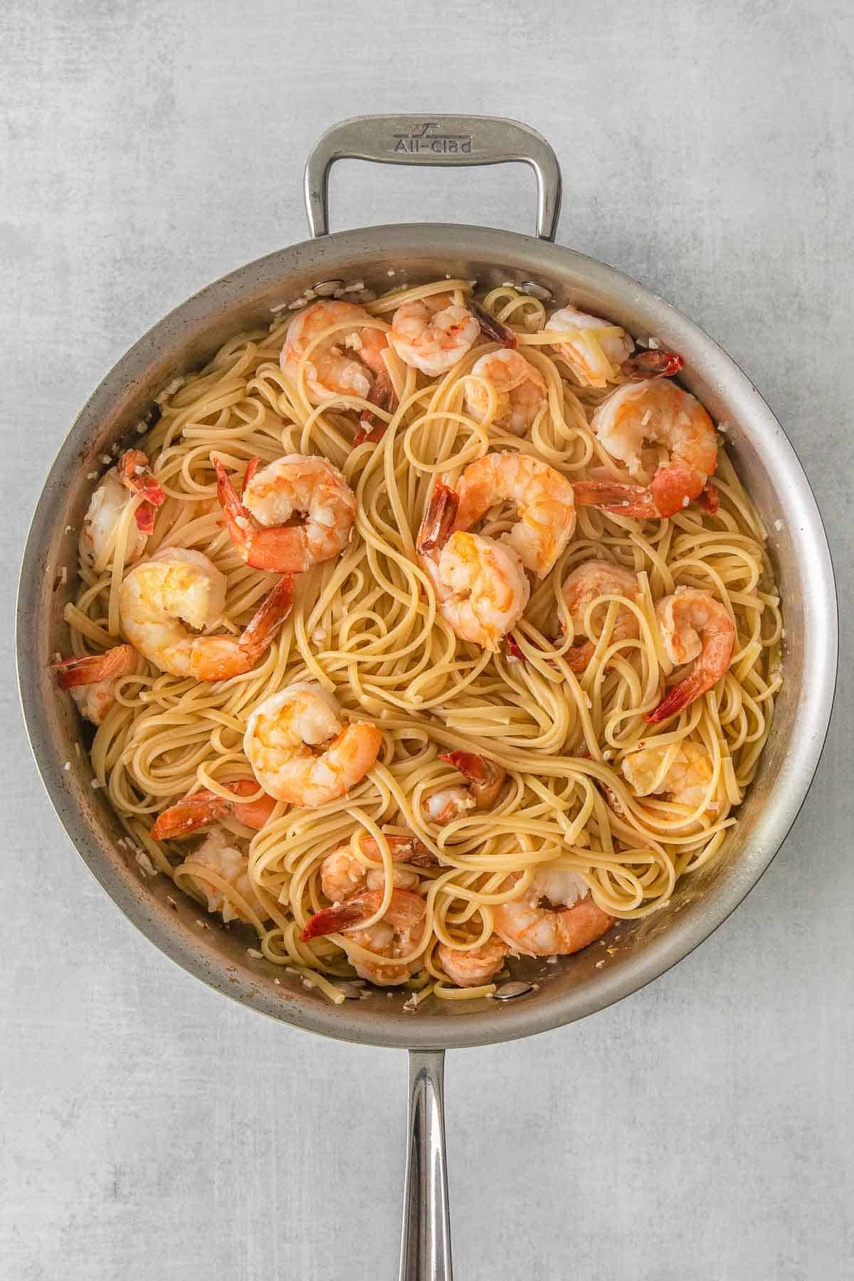 Stainless steel skillet with cooked shrimp over pasta.