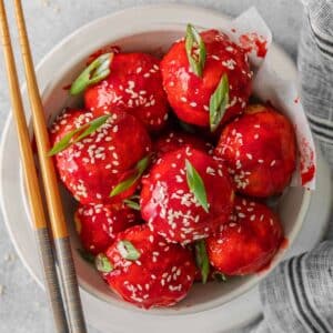 close up of sweet and sour chicken meatballs topped with sesame seeds and scallions.