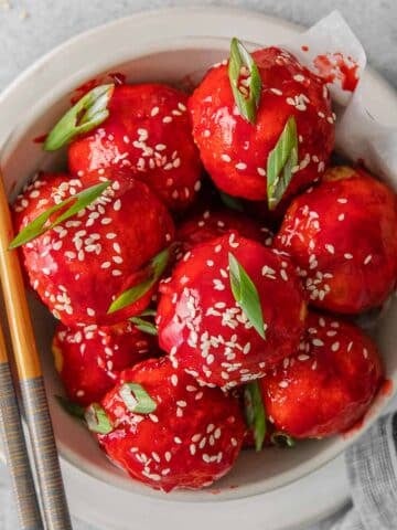 close up of sweet and sour chicken meatballs topped with sesame seeds and scallions.