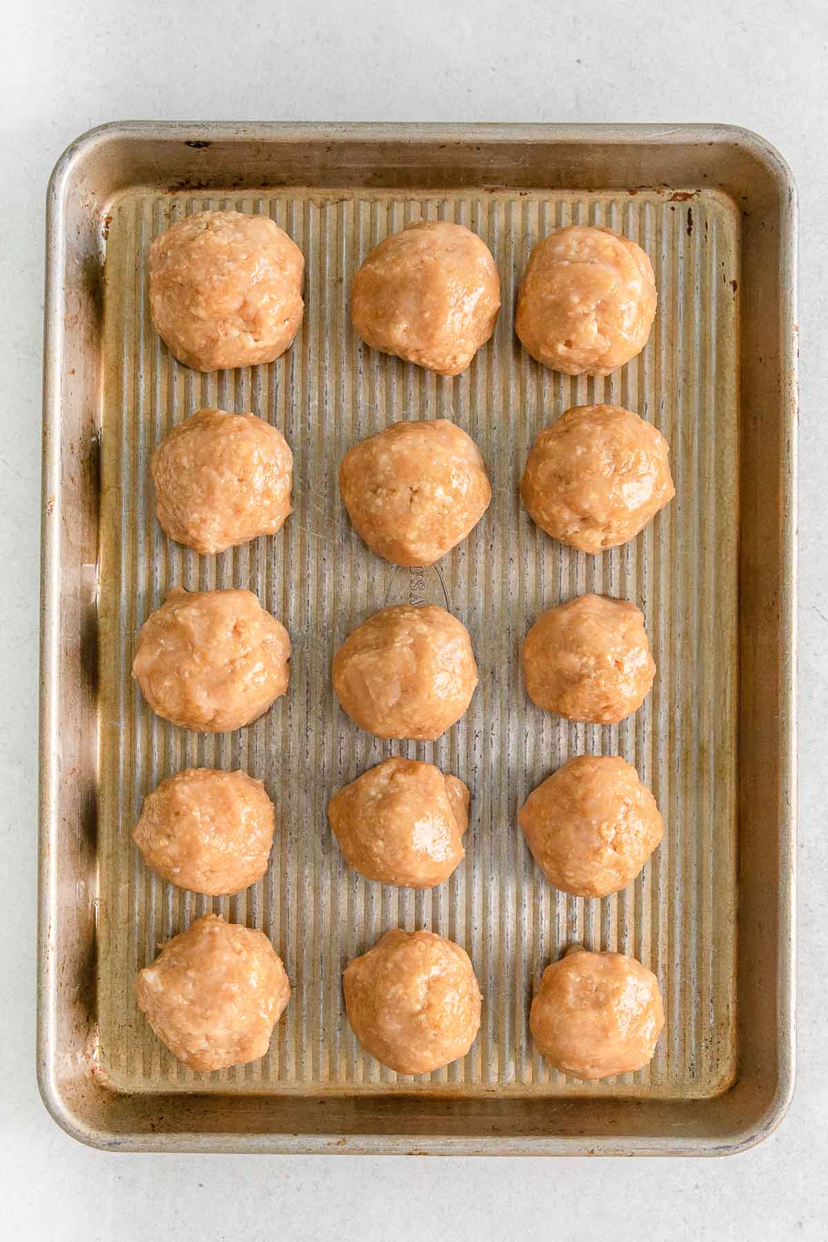 rolled chicken meatballs laid out on baking sheet.