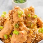 closeup of a white bowl of crispy bang bang chicken drizzled with creamy yum yum sauce.