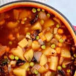 closeup of vegetable soup with mushrooms, peas and potatoes in a tomato broth.