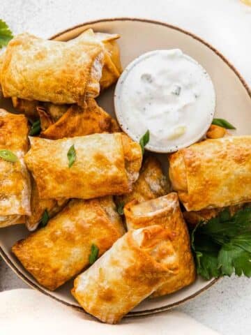 White plate of air fryer egg rolls topped with cilantro and a bowl of ranch on the side.
