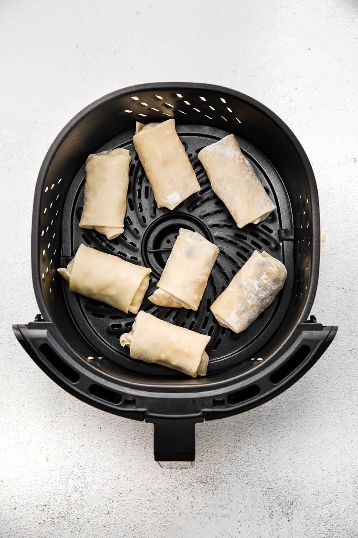 Uncooked egg rolls in air fryer tray.