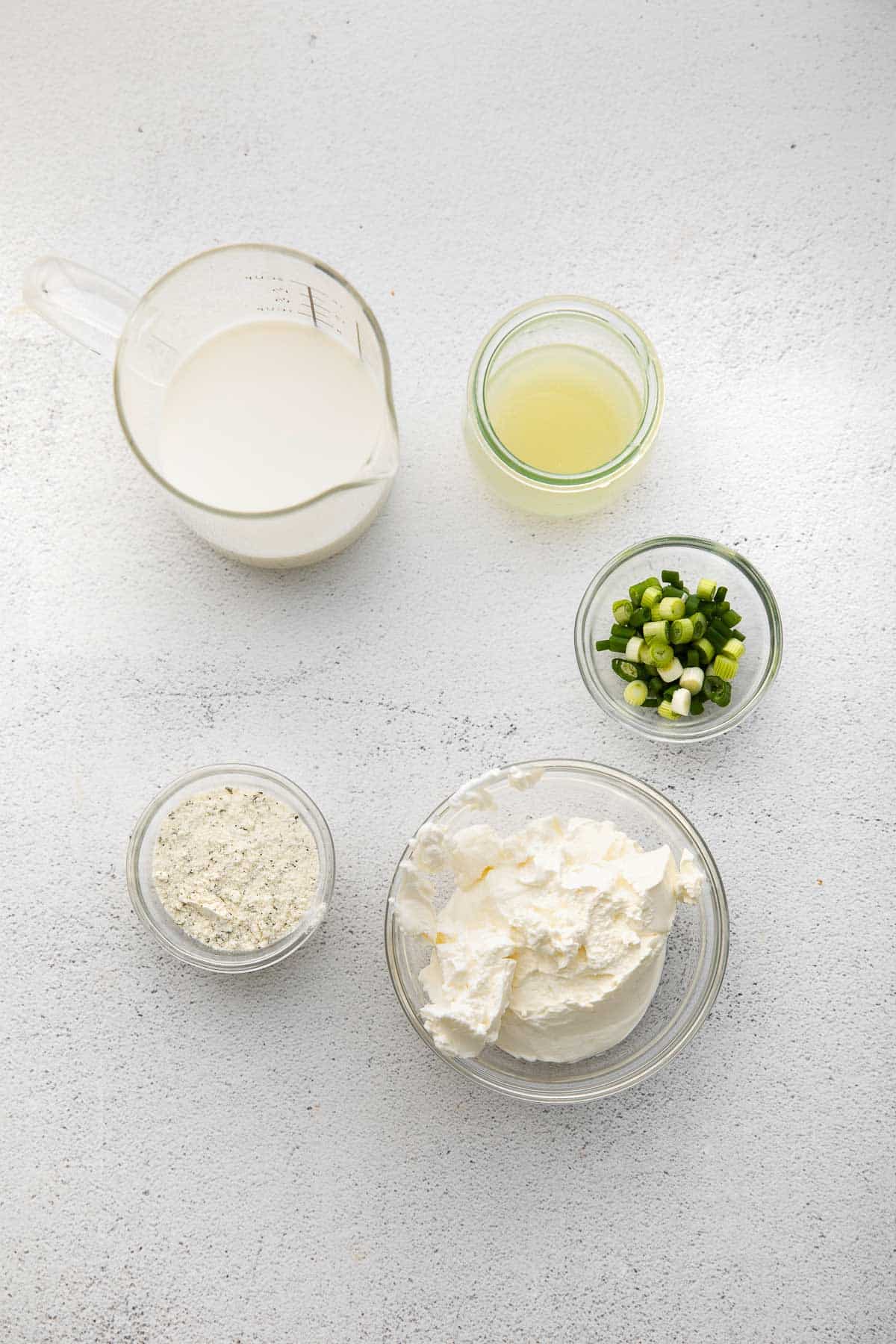 several bowls with ingredients for ranch dressing - sour cream, milk, ranch seasoning, lime juice and green onion.