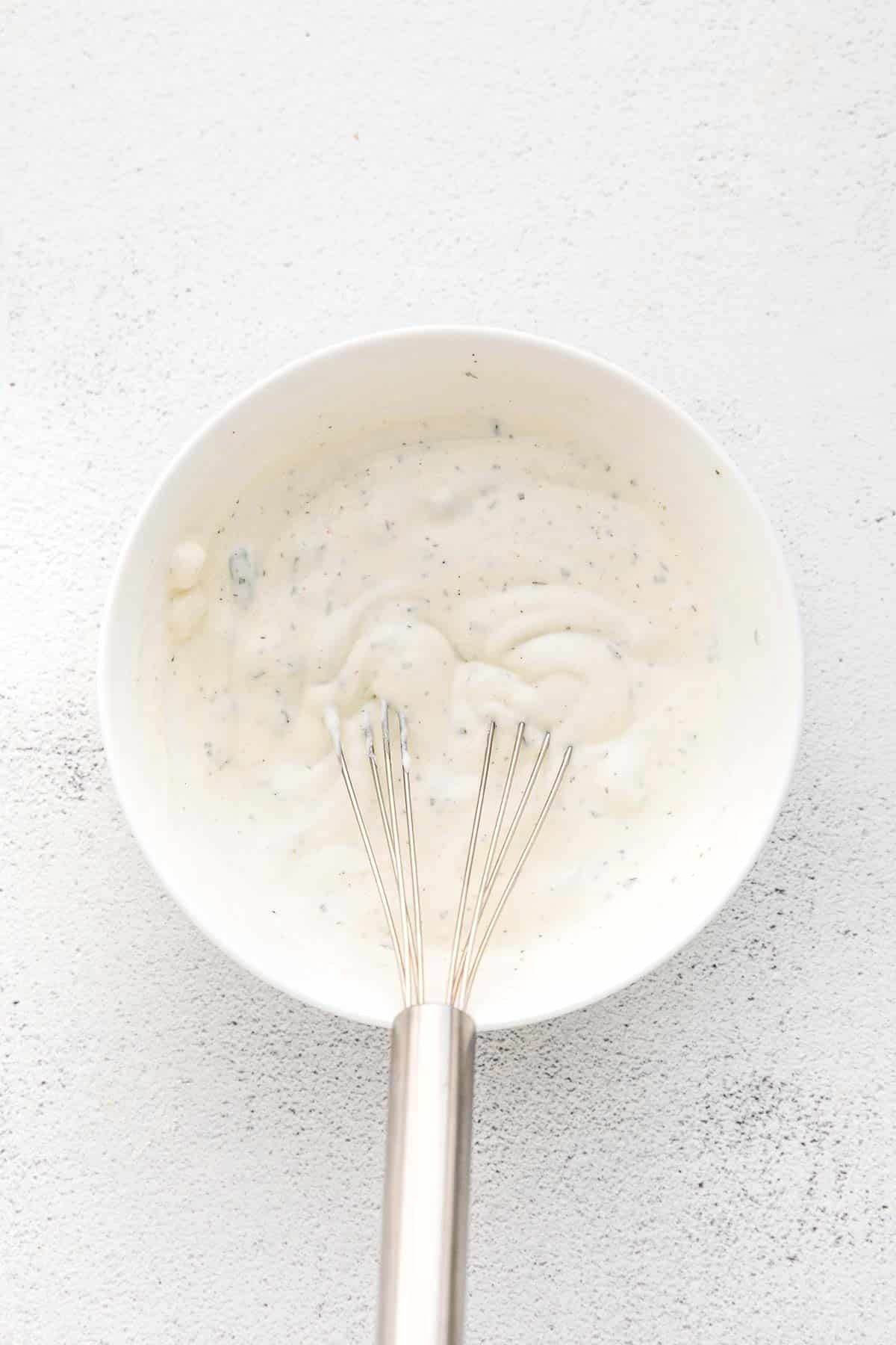 Medium white bowl with ranch dressing mix being whisked together.