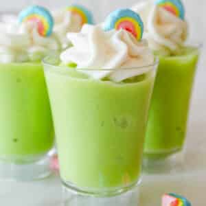 Close up of shot glass with green pudding topped with whipped cream and marshmallow.